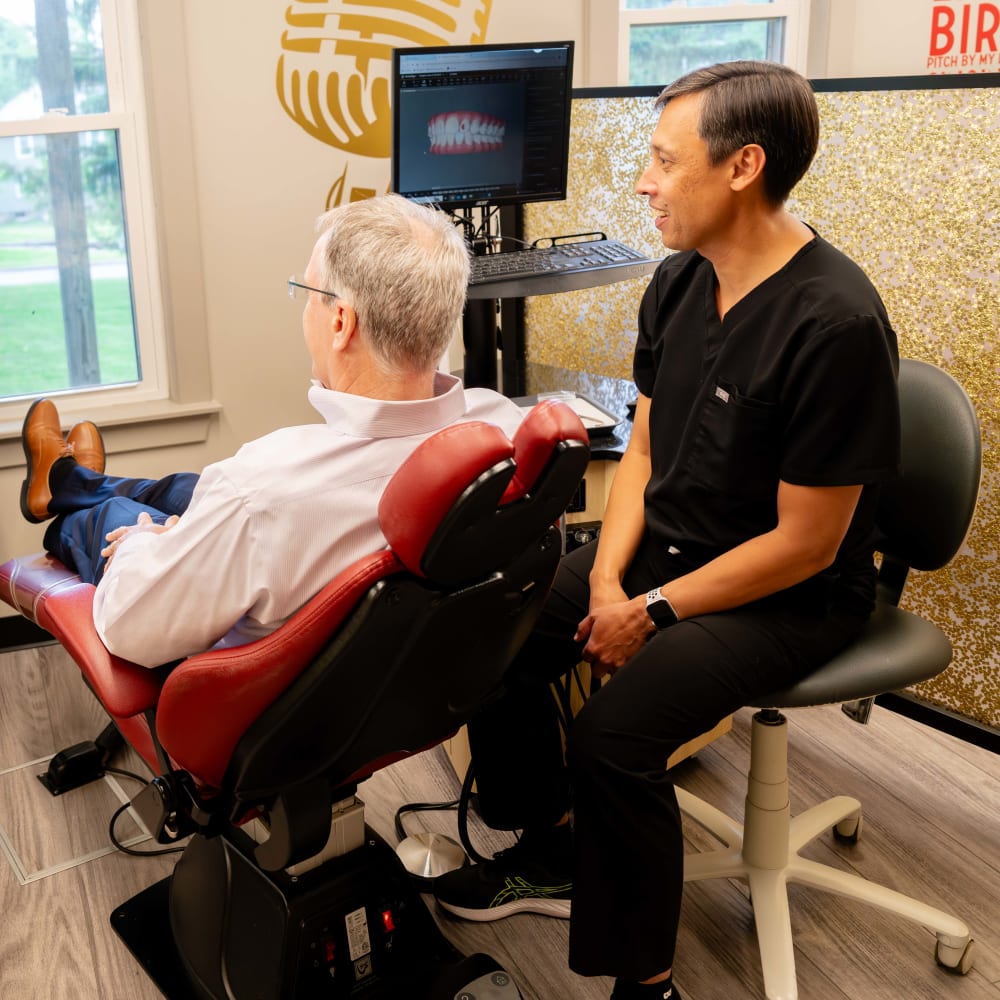 Dr. Sabelis sits beside a patient who is sitting in an exam chair. They are both looking at a Sturbridge Orthodontics team member, who is going over a 3D rendering of the patient's mouth.