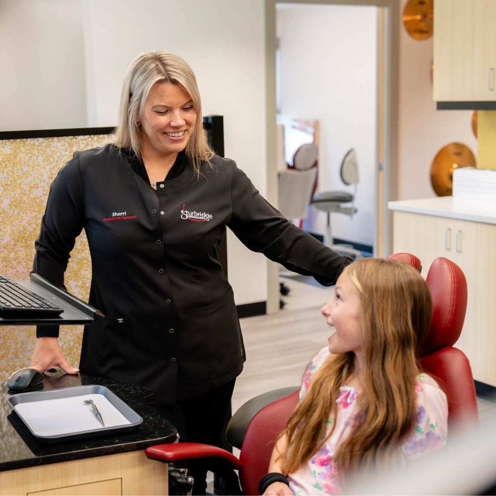 A team member at Sturbridge Orthodontics greets a young patient who is sitting in an exam chair.