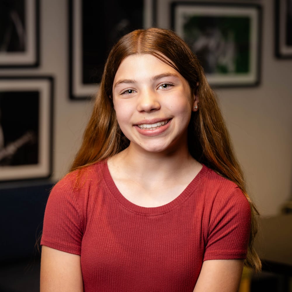 A teenage patient smiles at the camera, showing off straight teeth.